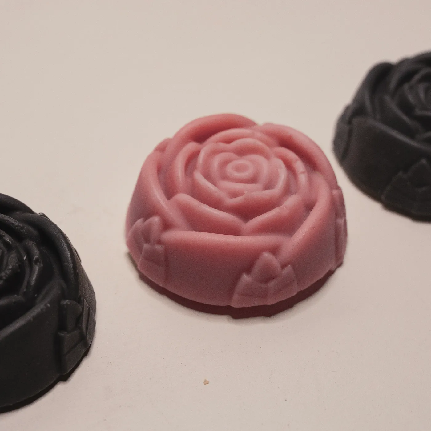 A pink rose-moulded soap between two charcoal rose soaps